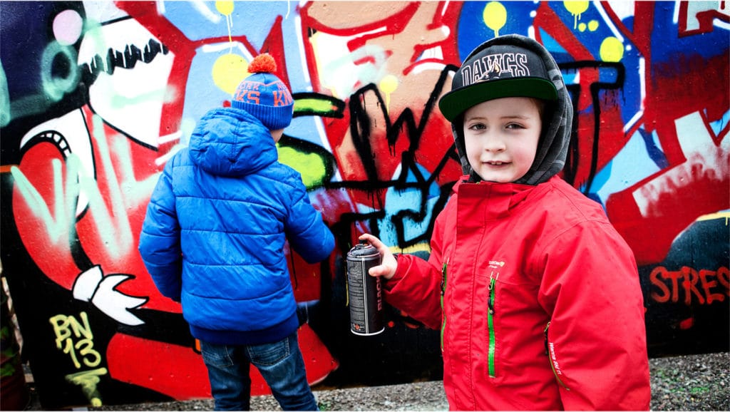 Barn med röd jacka framför en graffitimålning.
