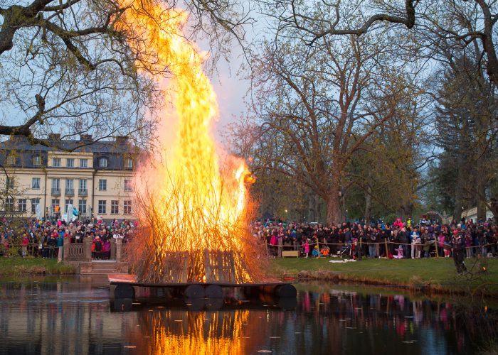 Valborgsbrasa på en flotte i vattnet med människor runtomkring som tittar