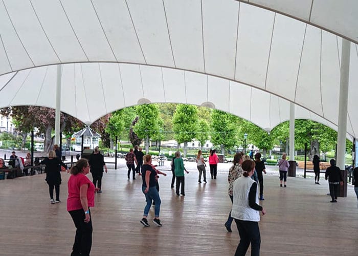 Personer dansar linedance på dansbana utomhus.